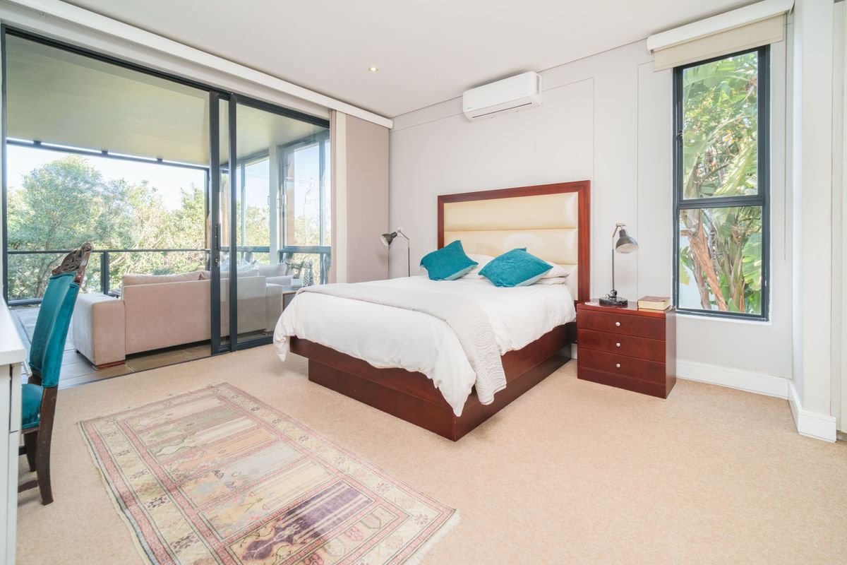 Spacious bedroom featuring neutral carpeting, a wall-mounted air conditioning unit, and large sliding glass doors providing direct access to a private balcony.
