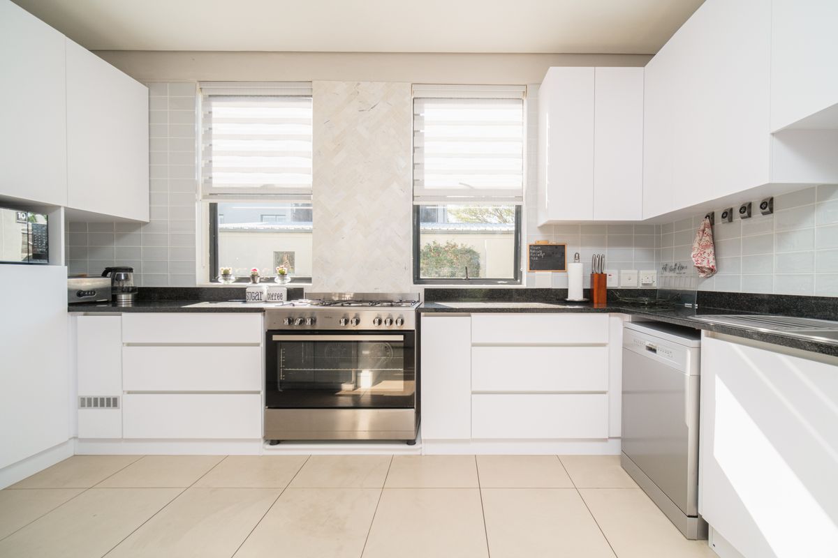 Modern kitchen featuring white cabinetry, dark granite countertops, tiled backsplash, and a stainless steel gas stove with oven.