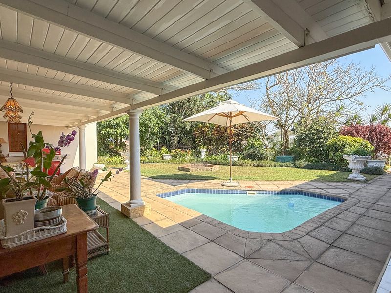 A spacious covered patio overlooking a private swimming pool and well-maintained garden area, perfect for outdoor relaxation and entertainment.