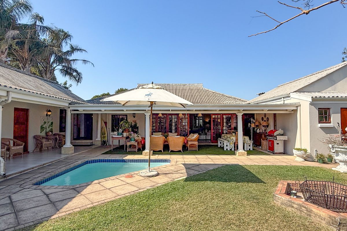 Spacious rear exterior featuring a swimming pool, covered patio area, manicured lawn, and a built-in brick fire pit, ideal for outdoor entertaining.