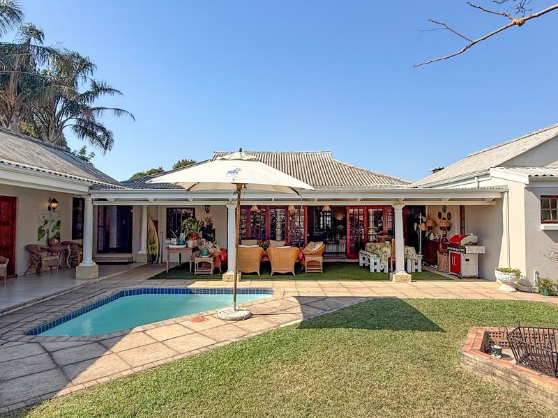 Spacious rear exterior featuring a swimming pool, covered patio area, manicured lawn, and a built-in brick fire pit, ideal for outdoor entertaining.