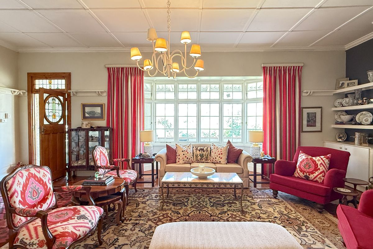 Spacious living room featuring a large bay window, coffered ceiling, hardwood floors, and a classic fireplace mantel with built-in shelving.