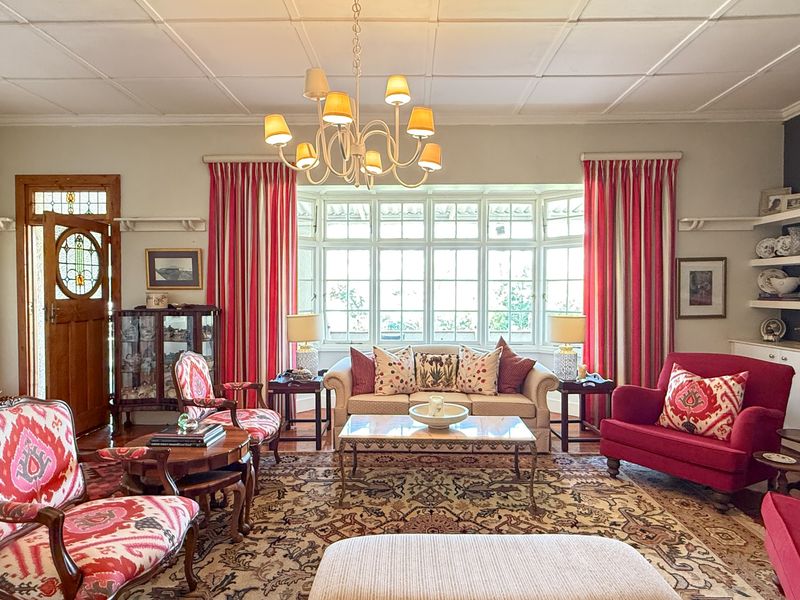 Spacious living room featuring a large bay window, coffered ceiling, hardwood floors, and a classic fireplace mantel with built-in shelving.
