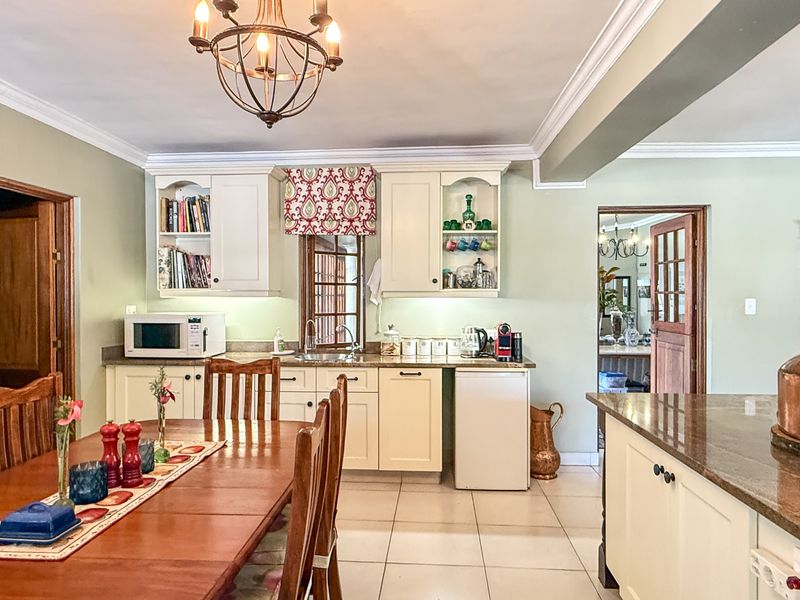 Open-plan kitchen and dining area featuring cream cabinetry, granite countertops, tiled flooring, and elegant crown molding throughout the space.