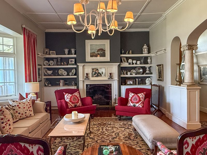A well-maintained living room featuring a classic fireplace, built-in shelving, elegant ceiling molding, and a large bay window providing natural light.