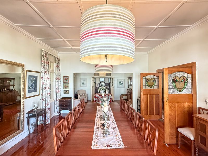 Spacious dining room featuring polished timber flooring, classic coved ceilings, and elegant stained glass timber doors leading to adjacent living areas.