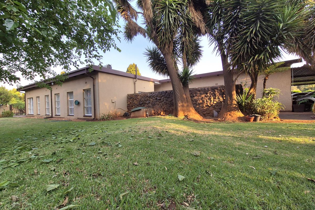 A view of the rear exterior of the house featuring a lawn, mature trees, and a stone retaining wall.