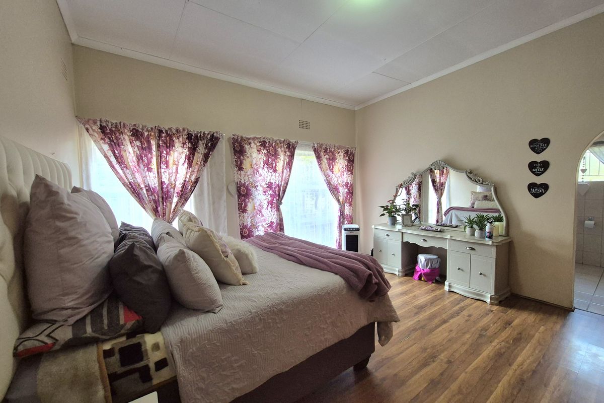 A spacious bedroom featuring wood-look flooring, large windows with natural light, and an arched doorway leading to an adjoining bathroom.