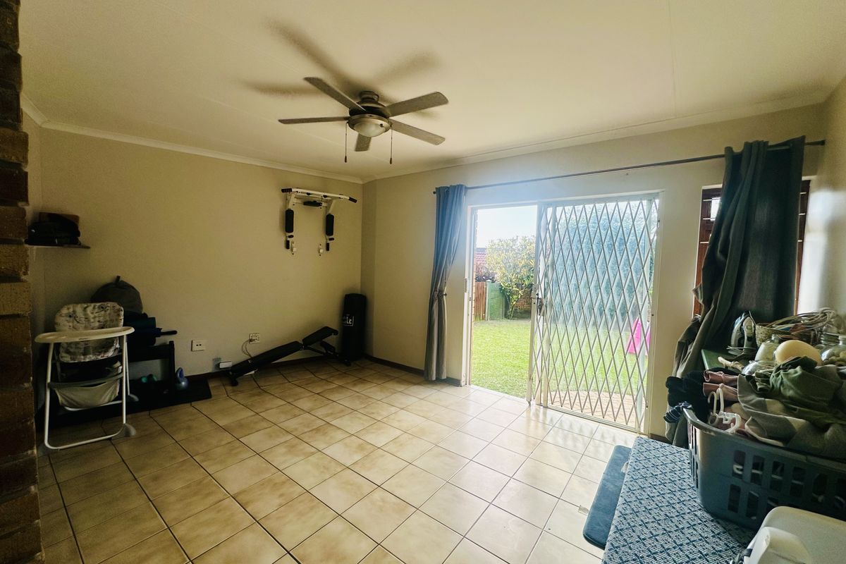 A living area featuring tiled flooring, a ceiling fan, and sliding glass doors with security gates providing direct access to the rear garden.