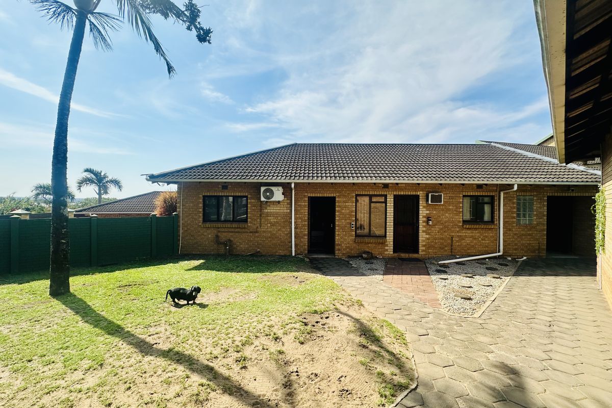 A rear view of a brick-faced house featuring a tiled roof, paved walkway, and a private garden area.