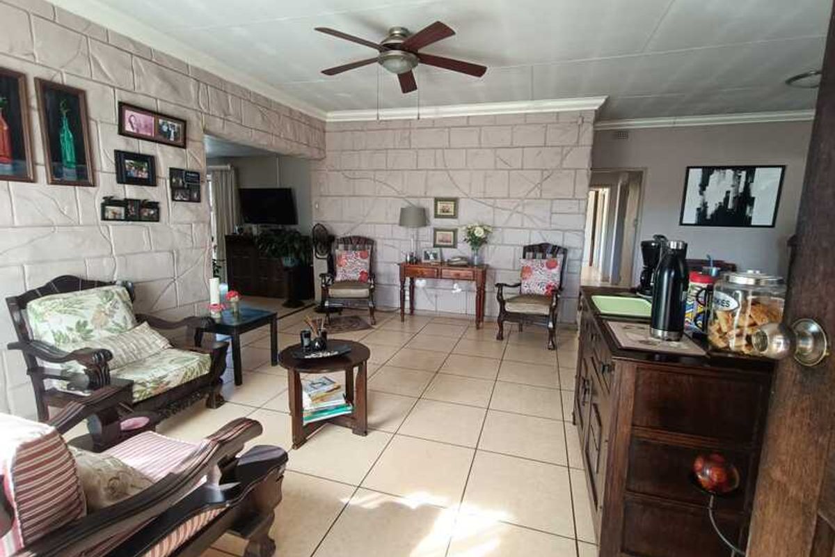 Spacious living area featuring textured stone-cladding feature walls, neutral ceramic floor tiles, and a ceiling fan.