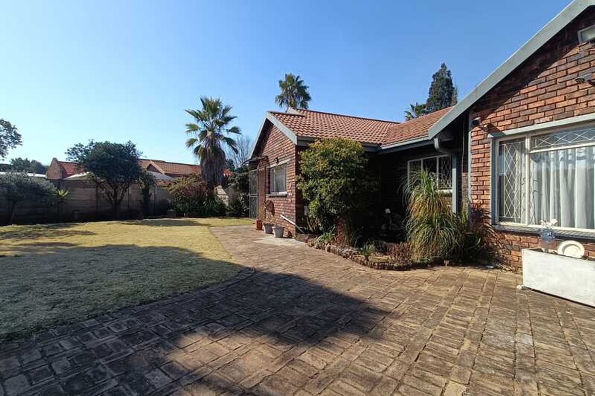 A view of the rear garden featuring a brick-paved patio area, established landscaping, and the rear facade of the brick house.