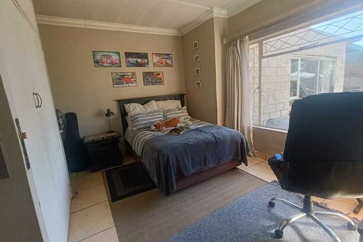 A bedroom featuring built-in cupboards, tiled flooring, and a large window allowing natural light, providing a functional and comfortable living space.