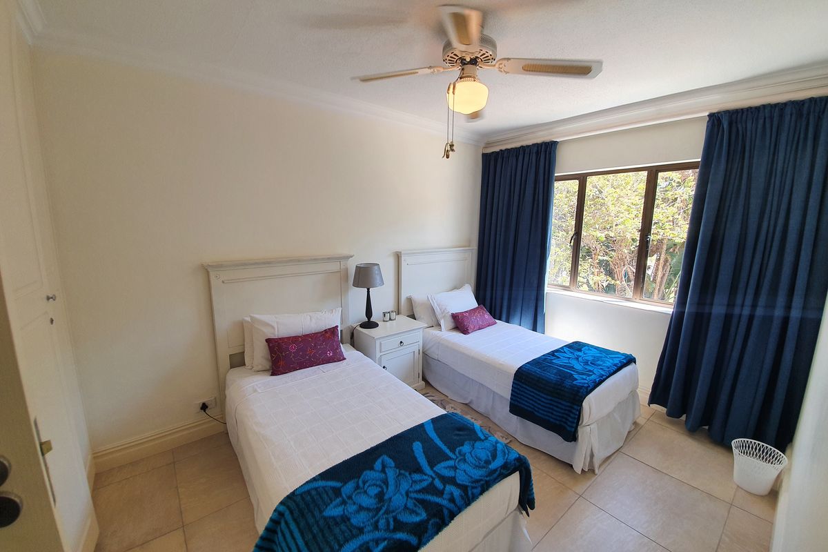 A well-maintained bedroom featuring tiled flooring, a ceiling fan, and large windows with curtains, providing a comfortable and functional living space.