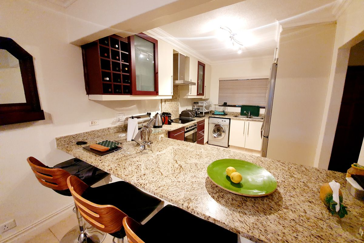 A functional kitchen featuring granite countertops, a breakfast bar, built-in cabinetry, an integrated extractor fan, and a built-in washing machine.
