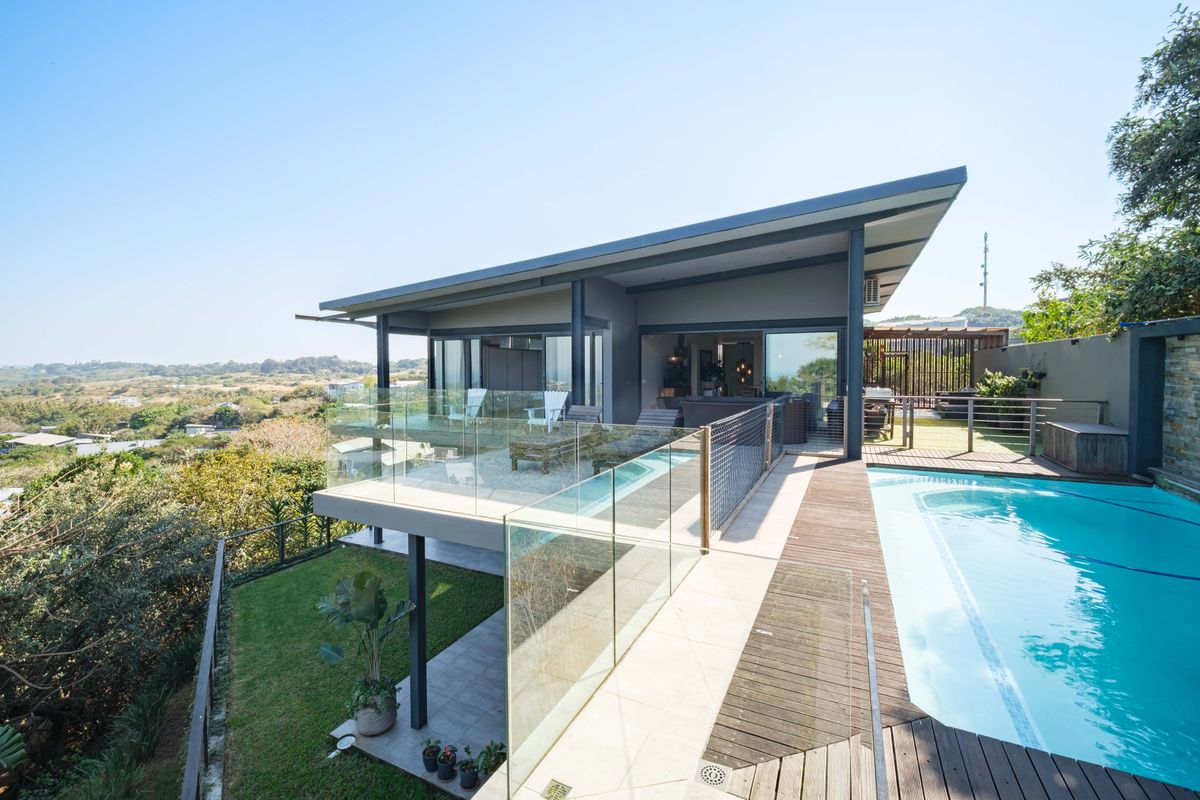 Modern architectural home featuring a spacious elevated balcony, glass balustrades, and a private swimming pool with timber decking overlooking the surrounding landscape.