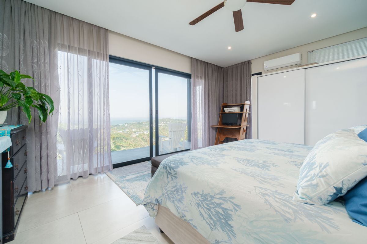 A bright bedroom featuring large sliding glass doors that open to a scenic balcony, built-in wardrobes, and a ceiling fan.