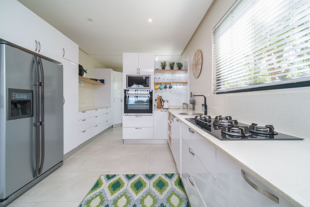 Modern kitchen featuring white cabinetry, stone countertops, a built-in oven, microwave, and a gas hob with a sleek black finish.