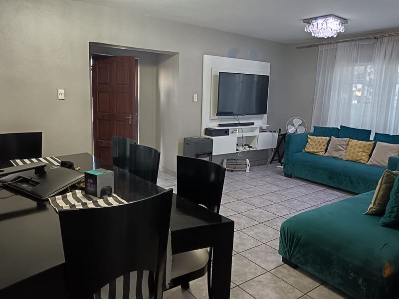 Open-plan living and dining area featuring tiled flooring, a built-in media console, and a decorative crystal chandelier.