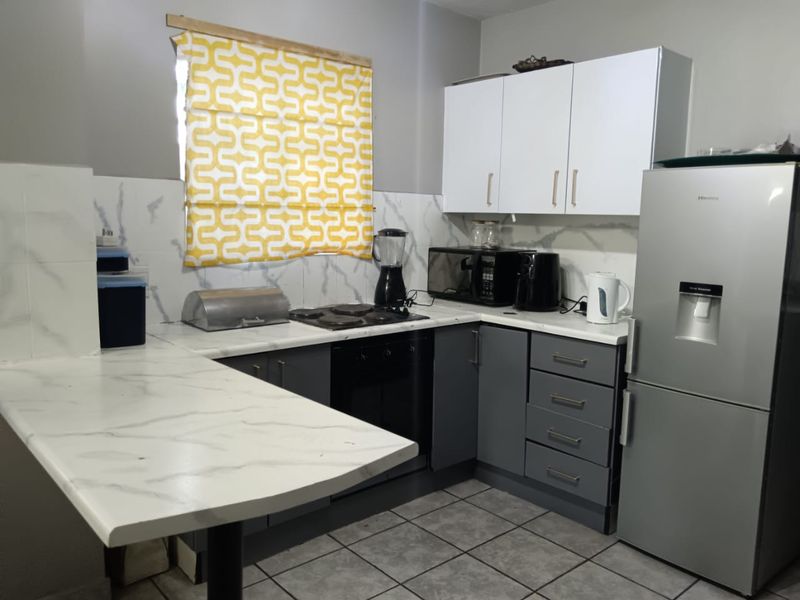 A functional kitchen featuring modern grey and white cabinetry, marble-look countertops, a tiled backsplash, and integrated cooking appliances.