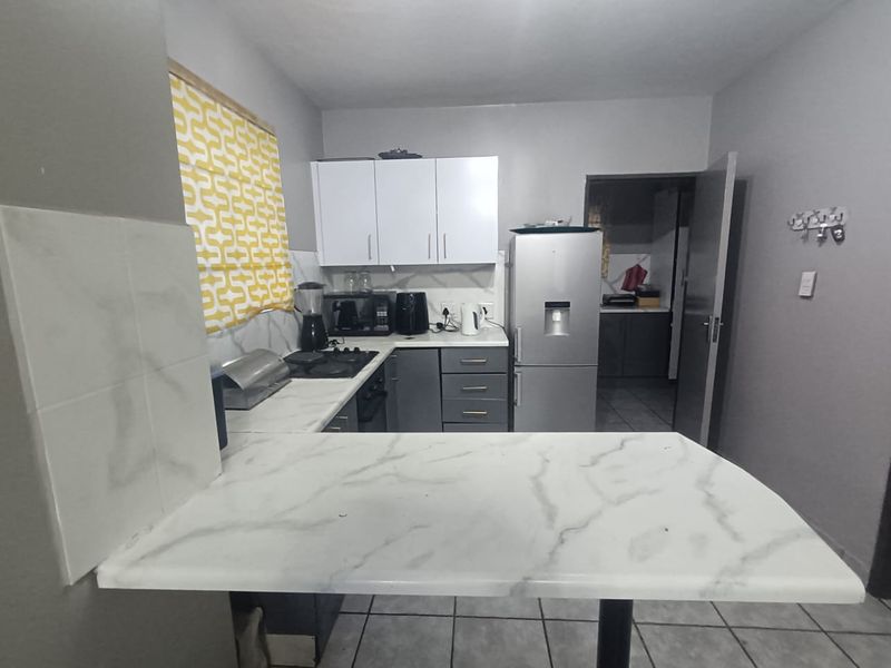 A functional kitchen featuring built-in cabinetry, marble-look countertops, a hob, and an oven, with an adjacent scullery area visible through the doorway.