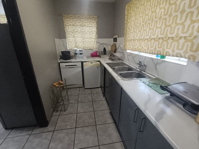 A functional scullery area featuring a double bowl sink, tiled backsplash, and built-in cabinetry with ample counter space for food preparation and utility tasks.