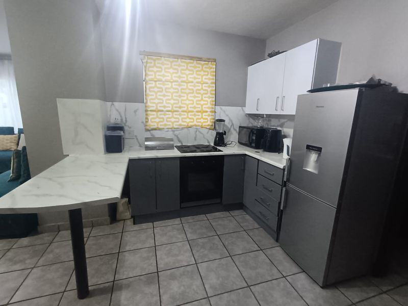 A functional kitchen featuring modern grey and white cabinetry, marble-look countertops and backsplash, and tiled flooring, providing a clean and practical cooking space.