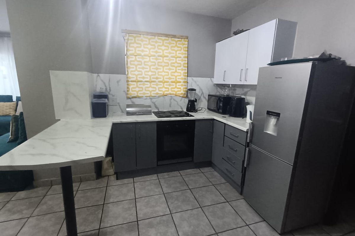 A functional kitchen featuring modern grey and white cabinetry, marble-look countertops and backsplash, and tiled flooring, providing a clean and practical cooking space.