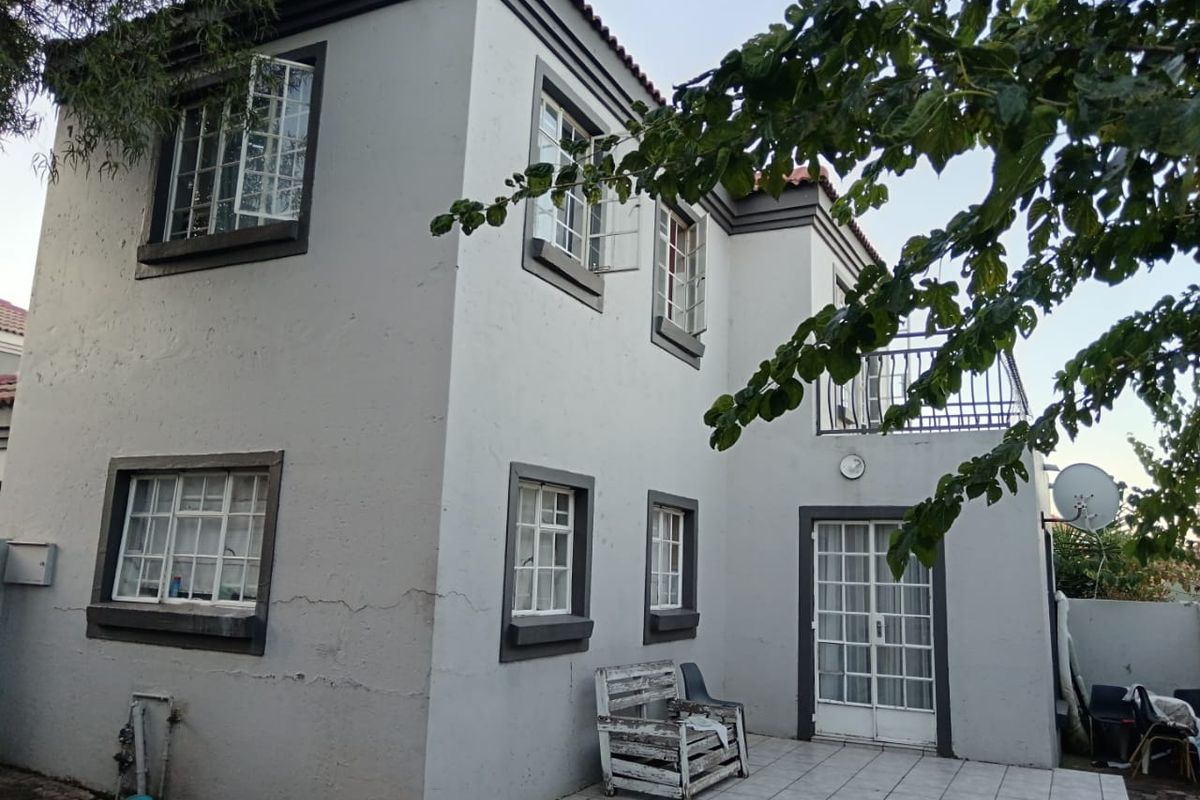 Rear view of a two-story house featuring a tiled patio, balcony with metal railings, and classic casement windows.