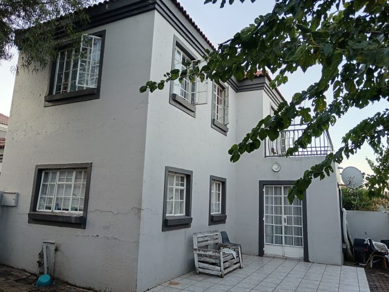 Rear view of a two-story house featuring a tiled patio, balcony with metal railings, and classic casement windows.