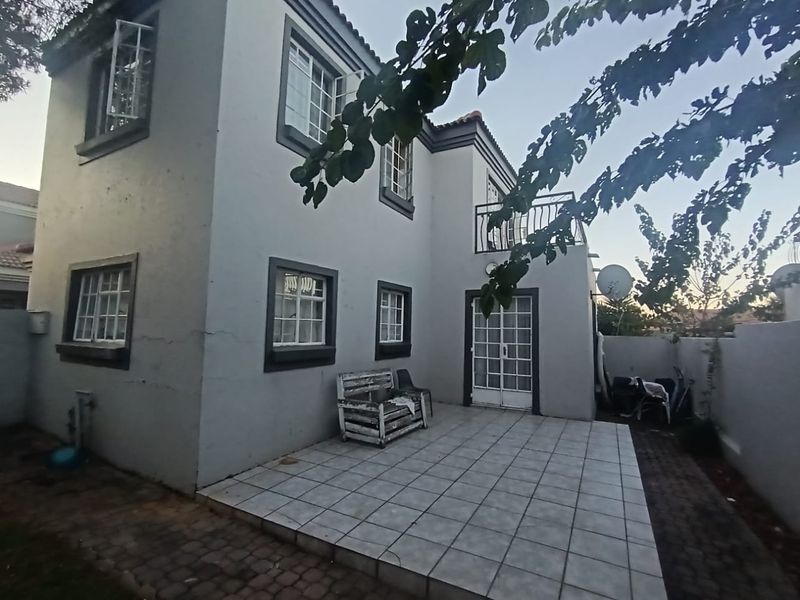 Rear view of a two-story house featuring a tiled patio, balcony, and paved outdoor area with classic casement windows and french door access.