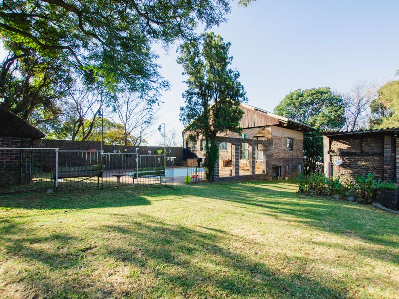 Spacious rear garden featuring a swimming pool, brick boundary walls, and mature trees, providing a private outdoor area for the property.