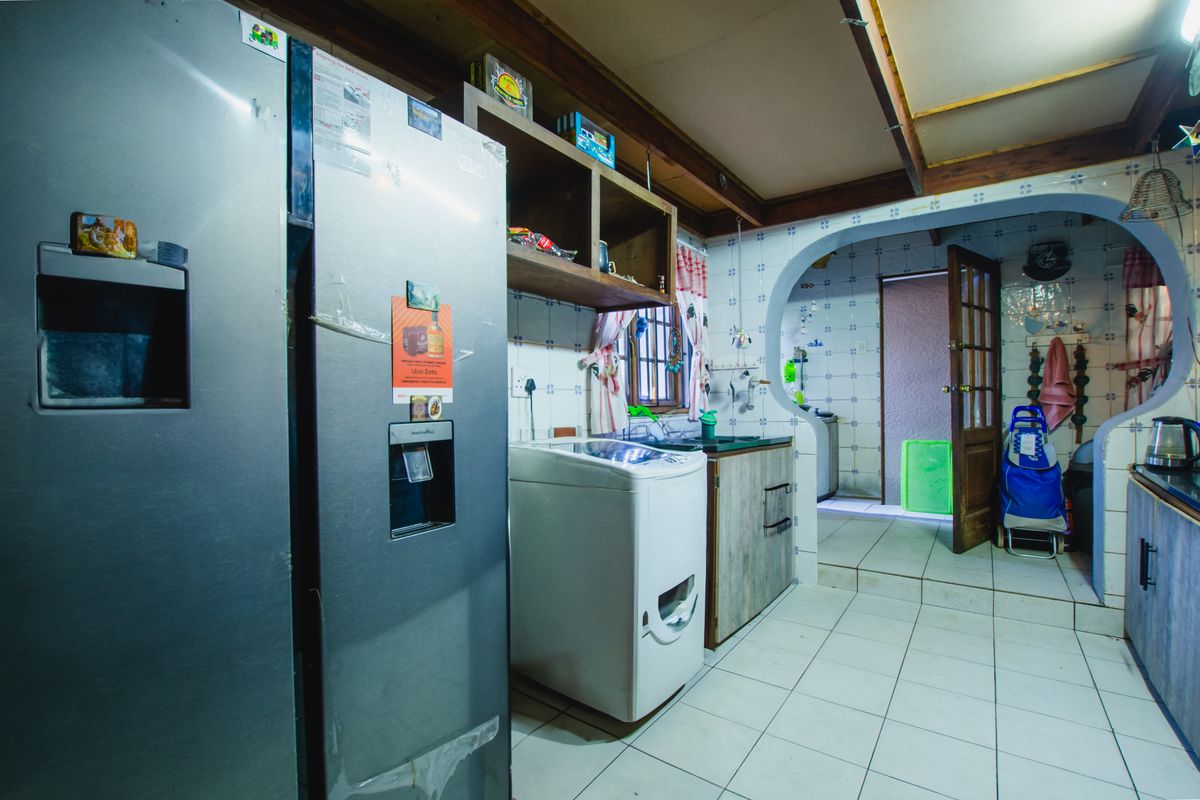 A functional kitchen and laundry area featuring tiled walls, built-in cabinetry, and an open-plan layout leading to an adjacent utility space.