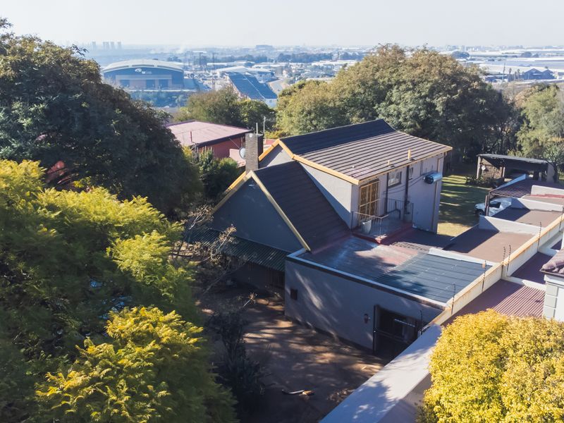An elevated aerial view of the property showing the roof structure, surrounding garden, and distant urban landscape.