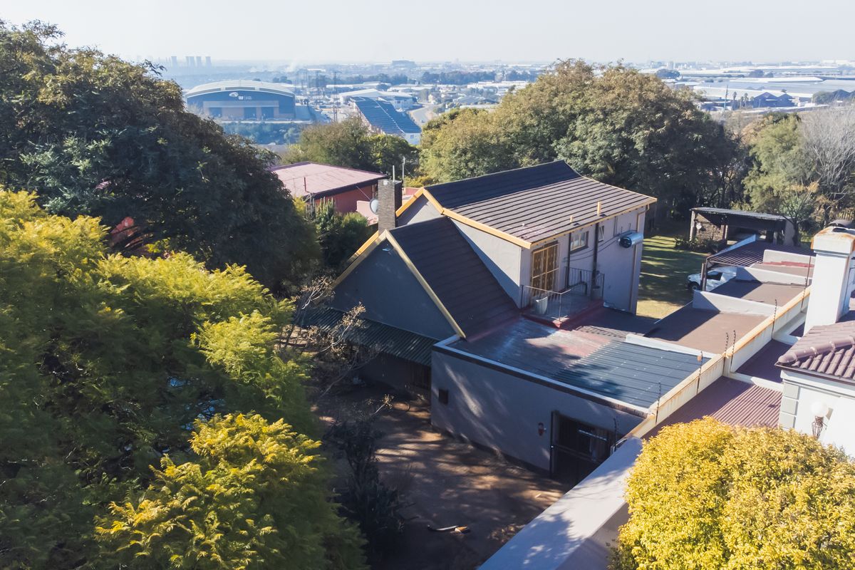 An elevated aerial view of the property showing the roof structure, surrounding garden, and distant urban landscape.