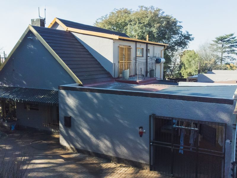 Rear view of the property featuring a multi-level roof structure, a small upper-level balcony, and a paved courtyard area with security gates.