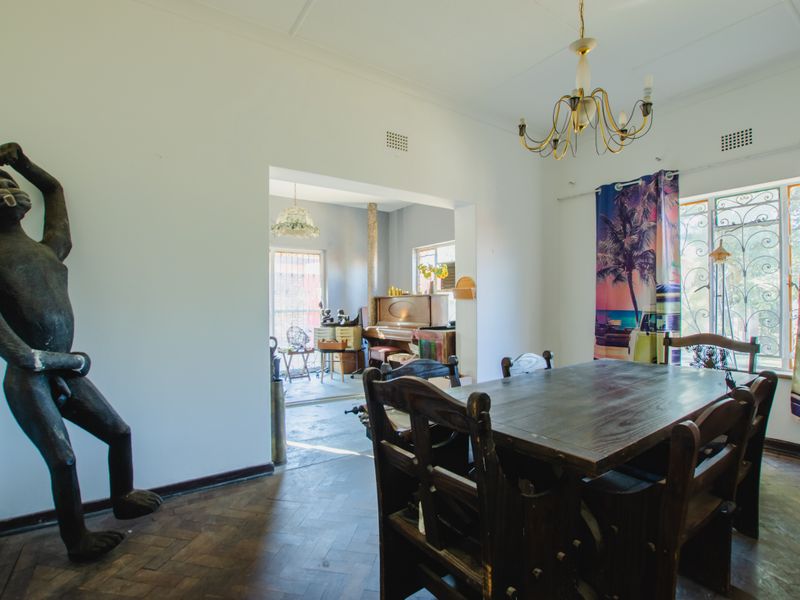 Dining room featuring classic parquet flooring, decorative chandelier, and an open-plan layout connecting to an adjacent living area with security bars on windows.