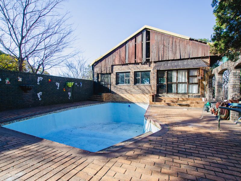Rear exterior view featuring a swimming pool, brick paved patio area, and a multi-level structure with timber cladding and brick facade.