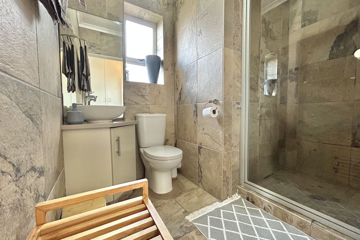 A compact bathroom featuring floor-to-ceiling stone-look tiling, a modern vessel sink vanity, a toilet, and a glass-enclosed shower.