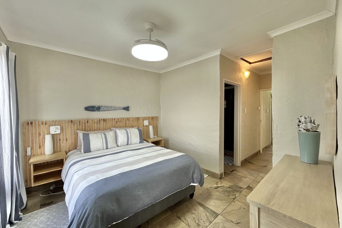 A bedroom featuring tiled flooring, a built-in wooden headboard, and a ceiling fan, providing a functional and neutral living space.