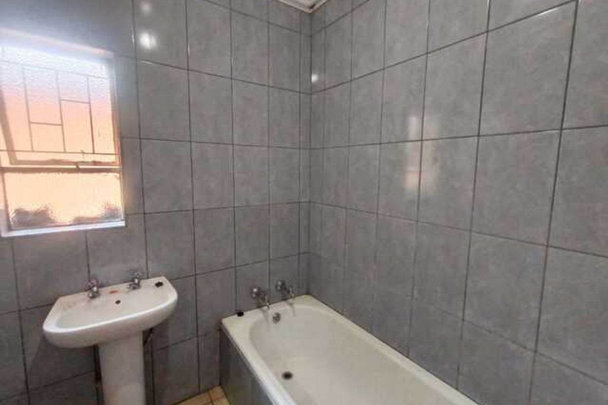 A functional bathroom featuring full-height wall tiling, a pedestal basin, and a standard bathtub with chrome fixtures.
