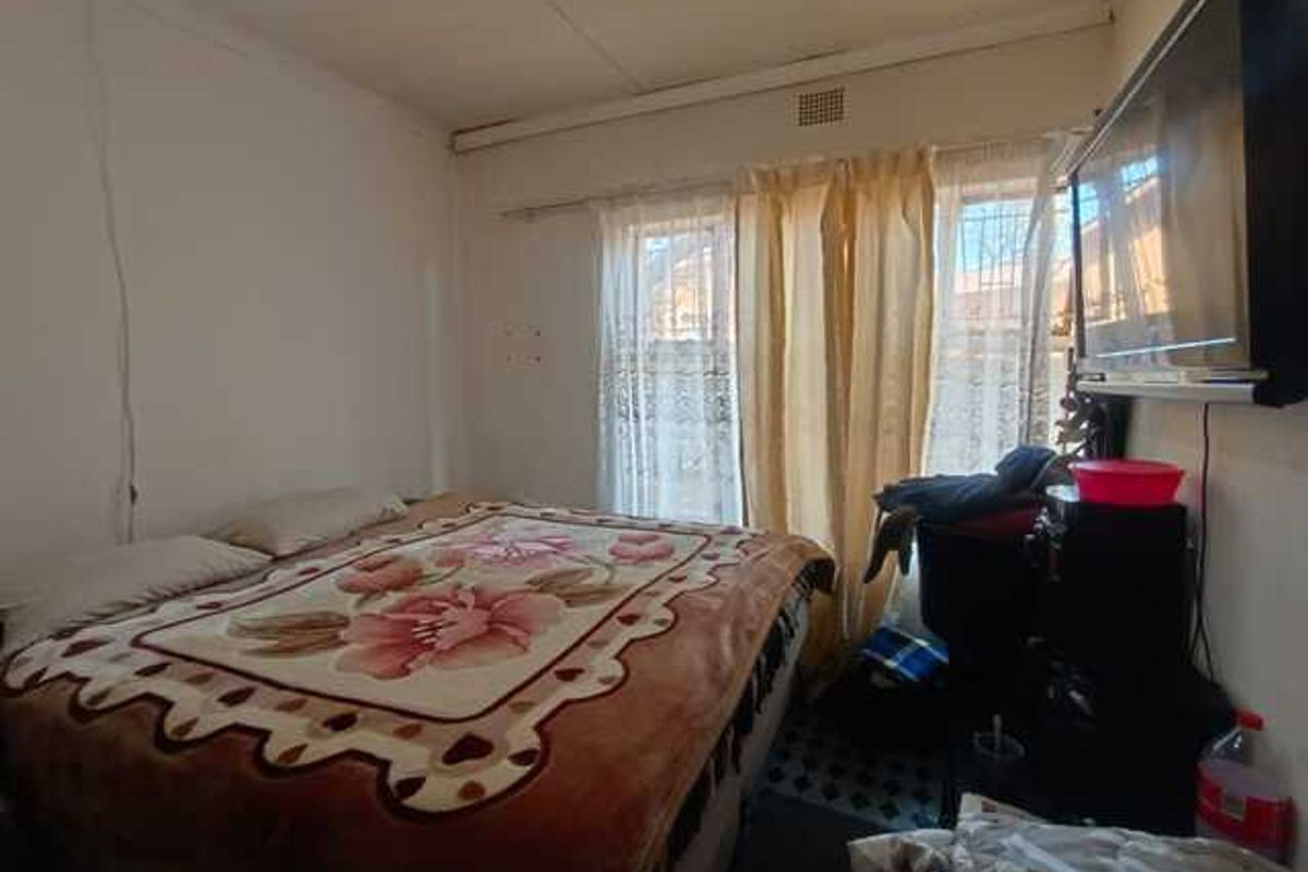 A compact bedroom featuring a window with curtain tracks and basic wall finishes.