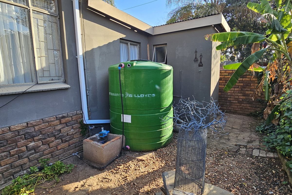 Exterior rear view showing a water storage tank installation with a pump, brick wall finish, and paved garden area.