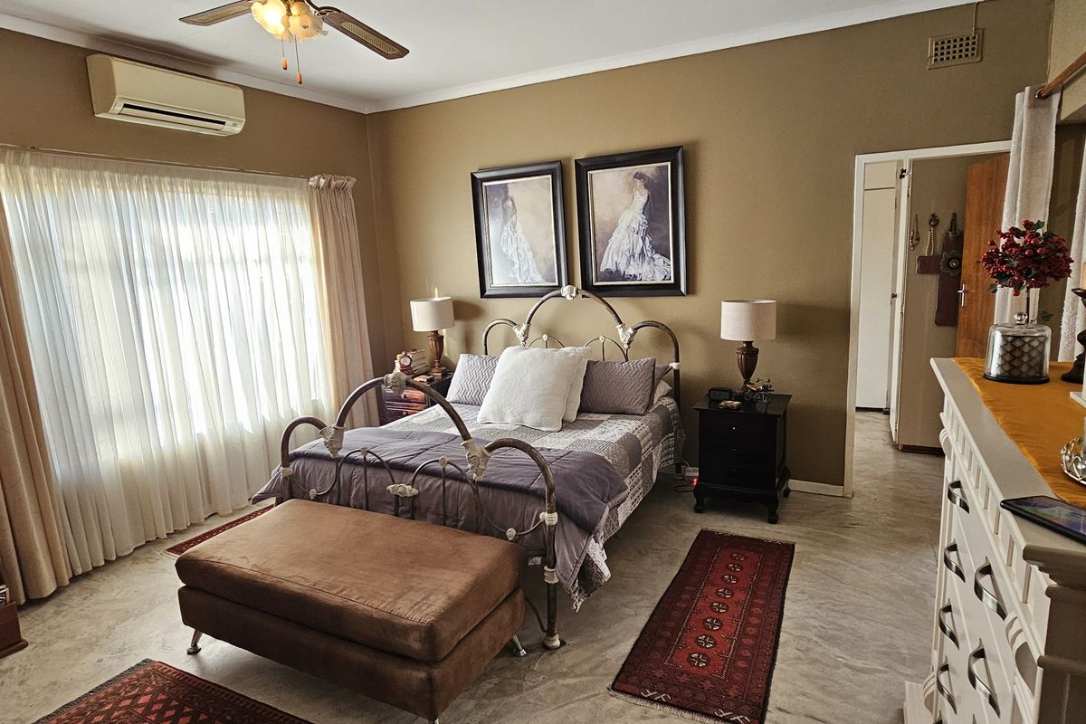 A well-maintained bedroom featuring tiled flooring, a wall-mounted air conditioning unit, and a ceiling fan.