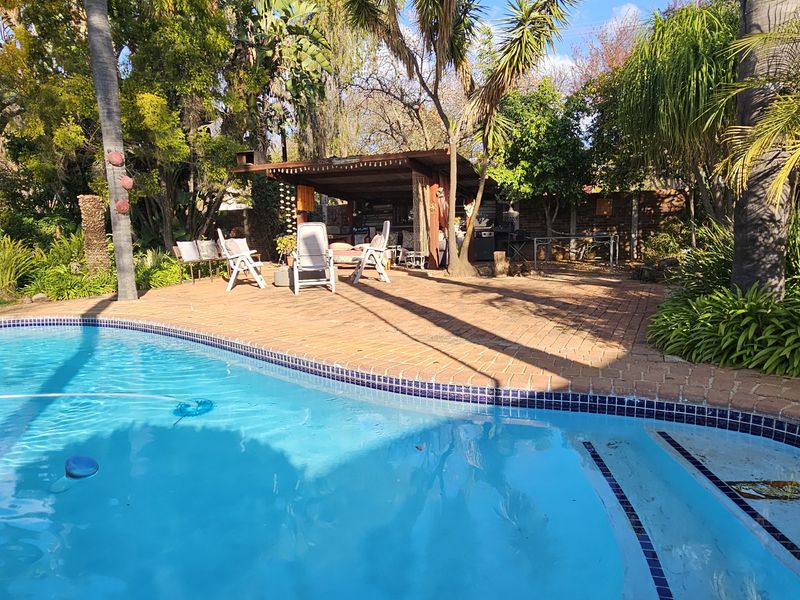 Outdoor pool area featuring a paved patio, established garden surroundings, and a covered entertainment space, ideal for relaxation and outdoor living.