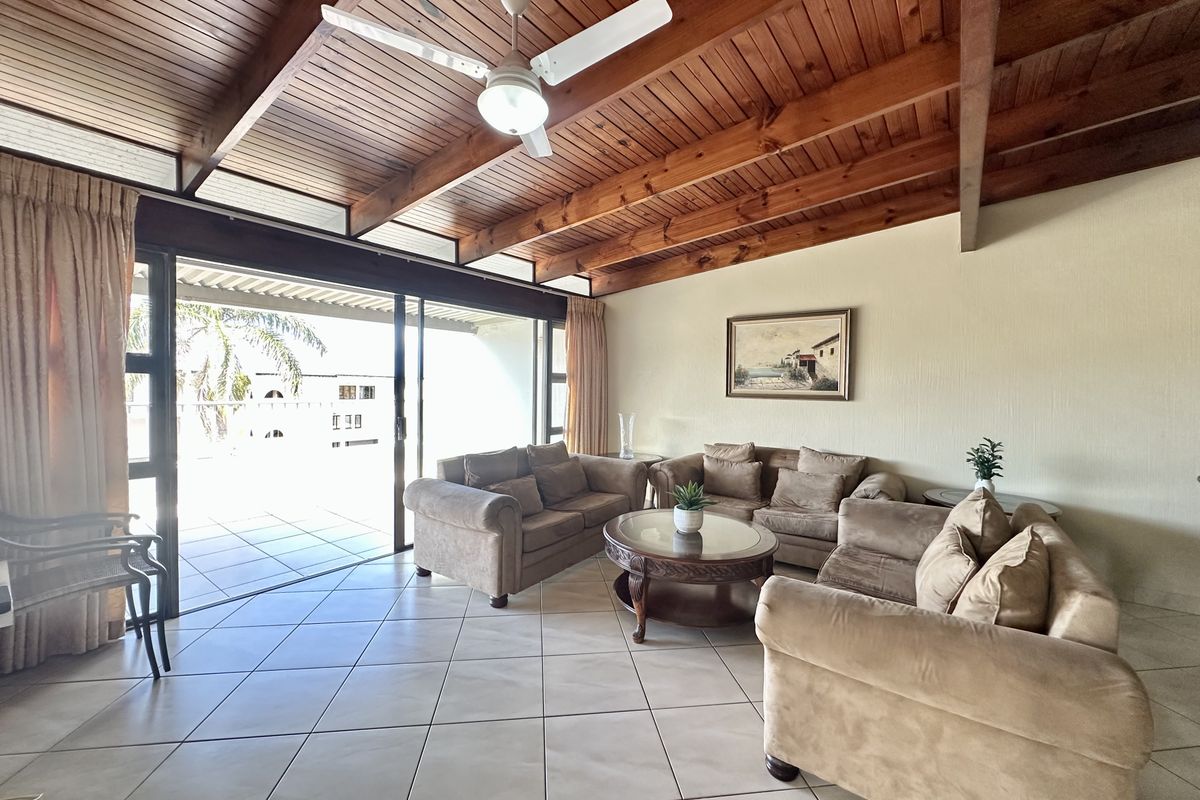 Spacious living area featuring a vaulted timber ceiling with exposed beams, ceiling fan, and large sliding doors opening to an outdoor patio.