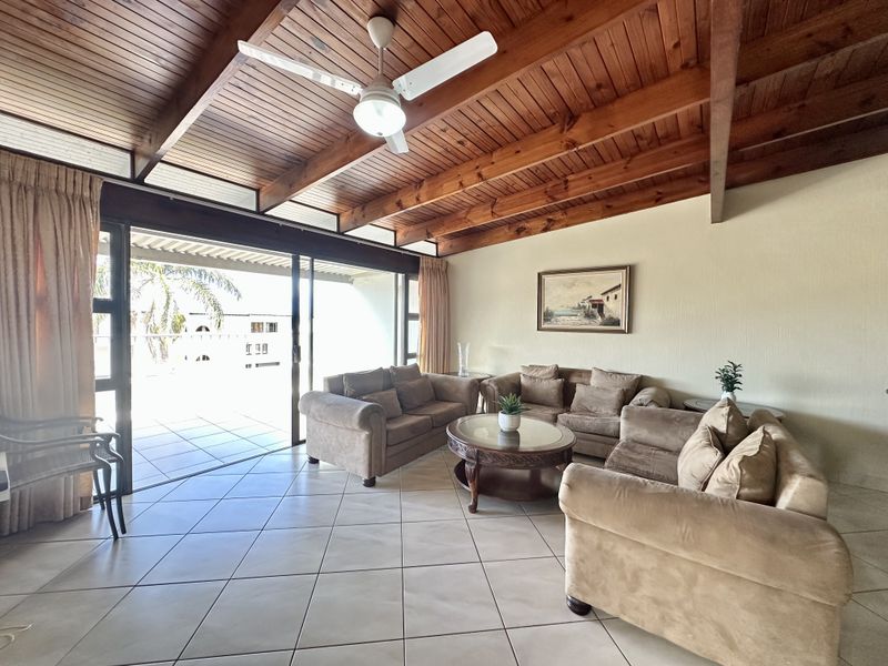 Spacious living area featuring a vaulted timber ceiling with exposed beams, ceiling fan, and large sliding doors opening to an outdoor patio.