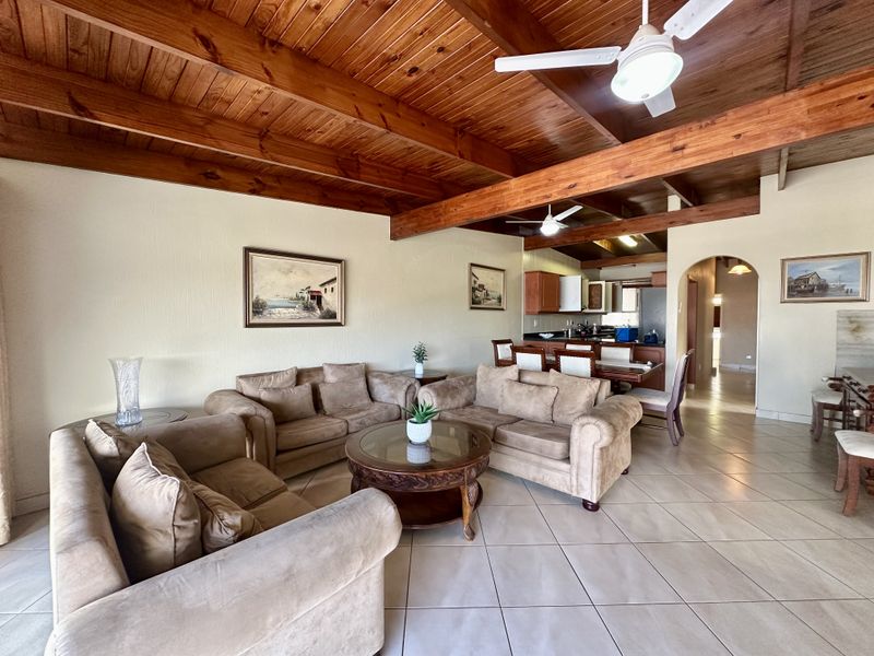 Spacious open-plan living and dining area featuring exposed timber beam ceilings, tiled flooring, and a seamless transition to the kitchen.