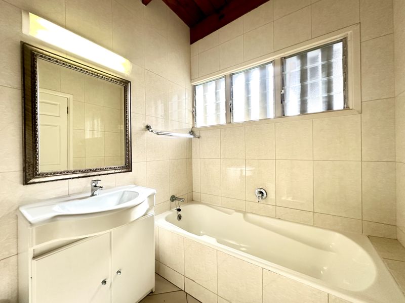A functional bathroom featuring a built-in vanity, bathtub with wall-mounted fixtures, and tiled walls with natural light from louvre windows.
