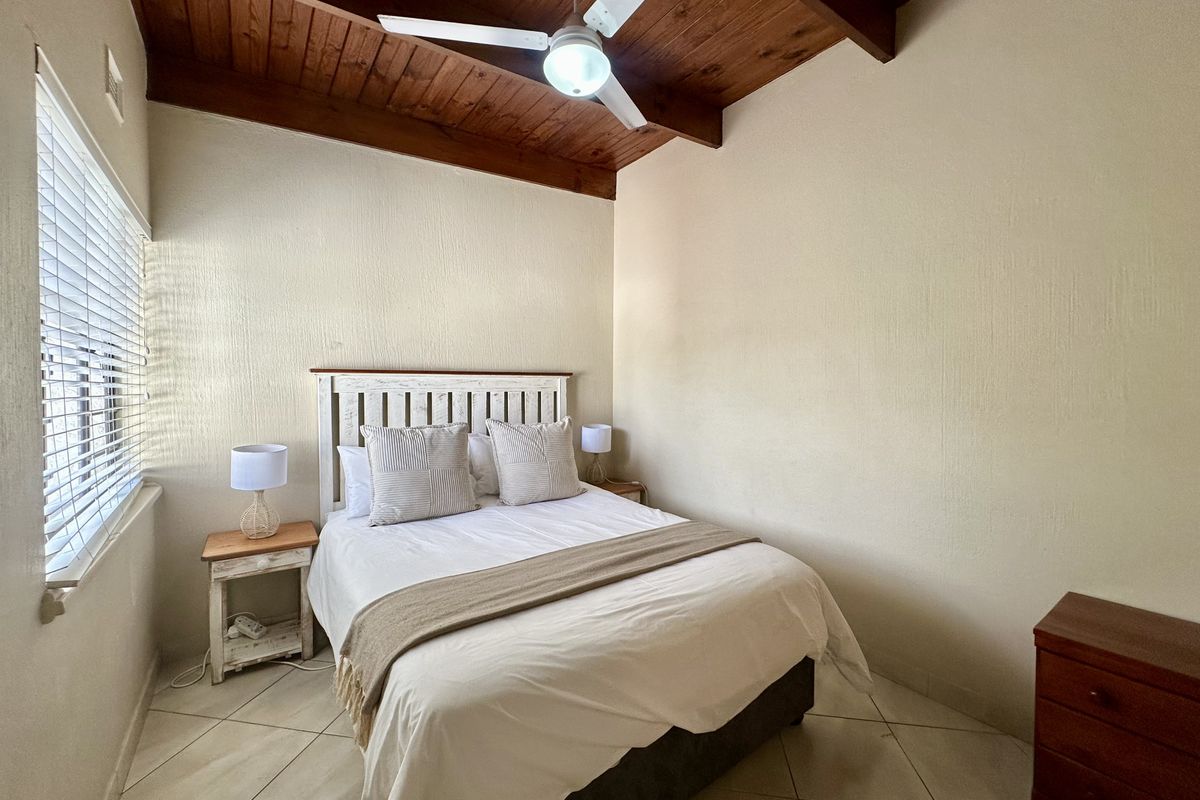 A cozy bedroom featuring a vaulted timber ceiling, ceiling fan, tiled flooring, and venetian blinds, offering a warm and functional living space.